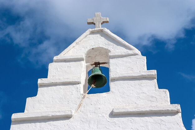 Photo bell tower with cross in mykonos, greece. chapel building detail architecture. white church on cloudy blue sky. religion and cult concept. summer vacation and travel on mediterranean island.