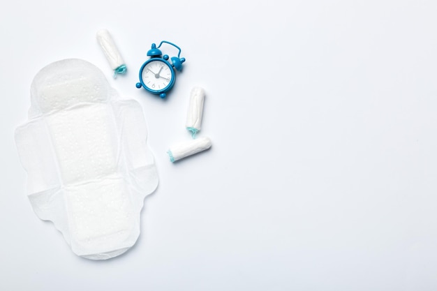 Bellende wekker met sanitaire vrouwelijke tampons en maandverband Medisch concept van kritieke dagen van de vrouw en menstruatie Vrouwelijke dagelijkse hygiëne Kopieer ruimte