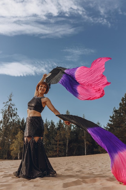 Belly dancer in kostuum dansen met fan sluiers zwaaien in de wind in de natuur