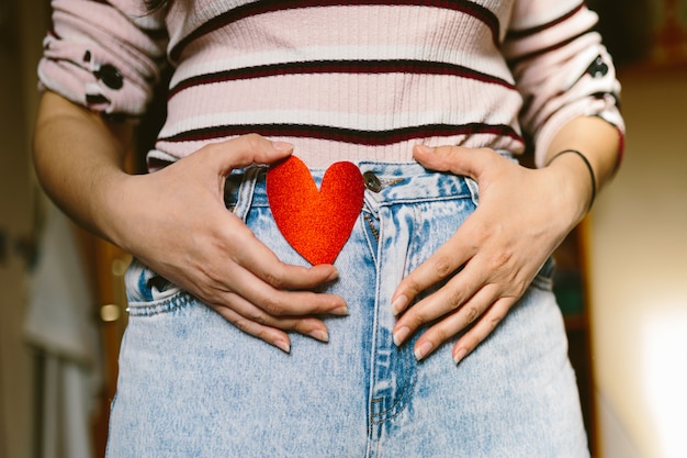 Belly of a newly pregnant woman with red glitter heart shaped cardboard. Important moment. Maternity concept.