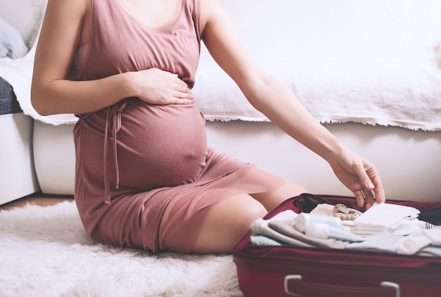 belly of pregnant woman in dress with travel bag of clothes and necessities mother during pregnancy