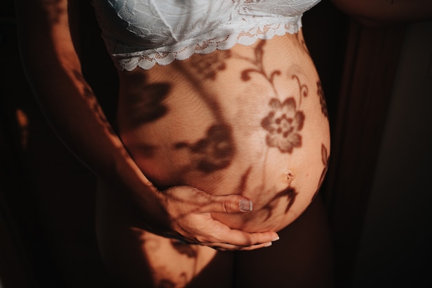 Belly of a pregnant woman with the shadow of some flowers