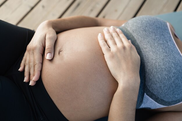 屋外でヨガをしている若い妊婦の腹のビュー-健康的なライフスタイルのためのスポーツエクササイズとマタニティコンセプト-トップハンドに焦点を当てる