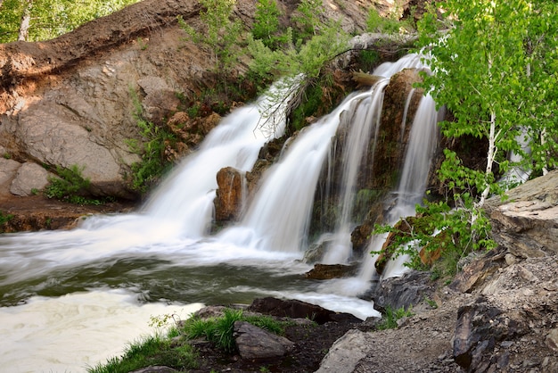 belovsky waterfall in the spring a small waterfall among the rocks surrounded by birch trees