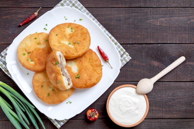 Belyashi  deepfried meat pies Patties on a plate on a wooden background with sour cream Top view