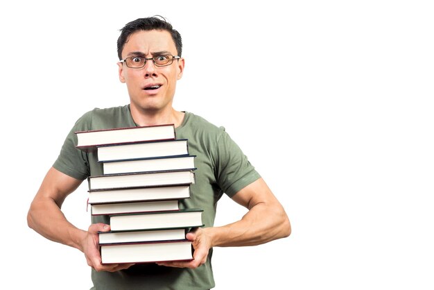 Bemused man in green t shirt and glasses frowning and looking at camera while carrying stack of textbooks against white background