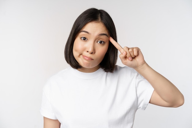 Ben je gek jonge aziatische vrouw rolt vinger op het hoofd en bespot iemand die dom staat in een t-shirt op een witte achtergrond?