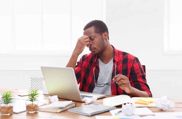 Benadrukt Afro-Amerikaanse werknemer met hoofdpijn werken met laptop op kantoor. Overstuur tijdens het werken aan een nieuw project, kopieer ruimte