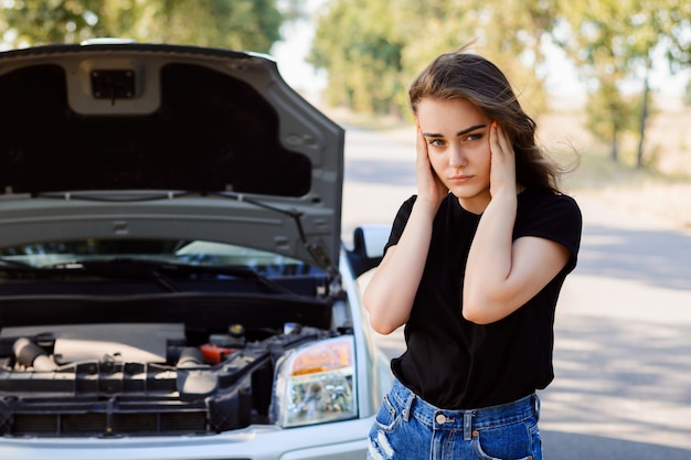 Benadrukt jong bestuurdersmeisje met een kapotte auto in het midden van nergens wachtend op hulp