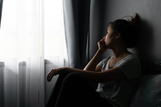 Benadrukt jonge aziatische vrouw die lijdt aan depressie en alleen op bed in een donkere kamer thuis zit.