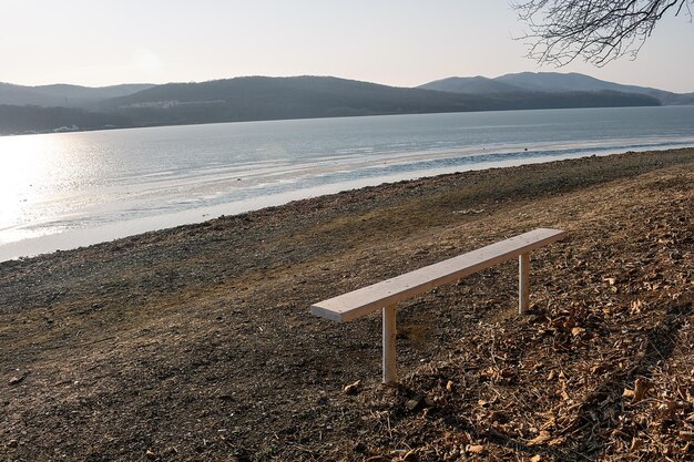 A bench on the shore of a lake with mountains in the background.