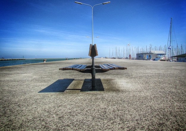 Bench and street light on walkway against blue sky