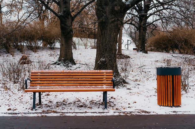 A bench and a trash can are in a park.