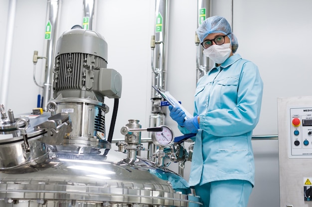 사진 파란색 실험실 유니폼을 입은 구부러진 과학자는 손에 있는 압축기 엔진 태블릿 근처에 서서 카메라를 봅니다.