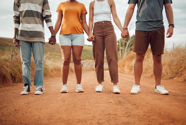 Benen diversiteit en mensen die elkaars hand vasthouden in solidariteitsverbinding of ondersteuning Vertrouw vriendschapshulp en buiten woestijn groepsteam of vrienden lopen reizen of staan op onverharde plattelandsweg