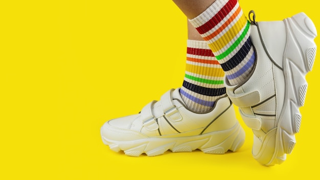 Benen met meerkleurige sokken in het zicht van regenboog in witte sneakers op gekleurde achtergrond, close-up, lgbtq, trots, copyspace