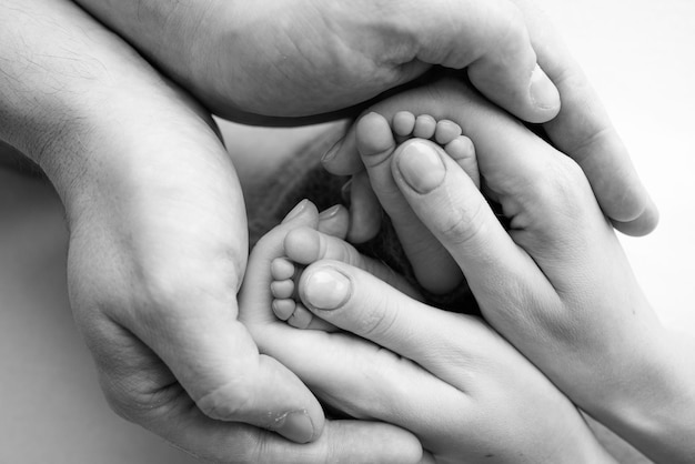 Benen, tenen, voeten en hielen van een pasgeborene Met de handen van ouders houdt vader moeder zachtjes de benen van het kind vast Macrofotografie close-up Zwart-wit foto Hoge kwaliteit foto
