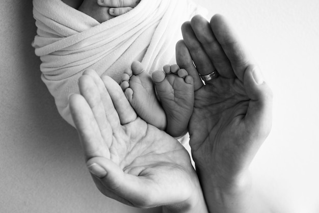 Benen, tenen, voeten en hielen van een pasgeborene Met de handen van ouders houdt vader moeder zachtjes de benen van het kind vast Macrofotografie close-up Zwart-wit foto Hoge kwaliteit foto