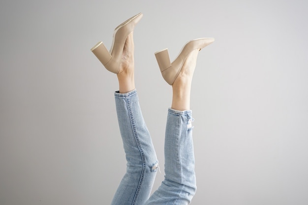 Benen van een jonge vrouw in jeans en schoenen op grijze achtergrond.
