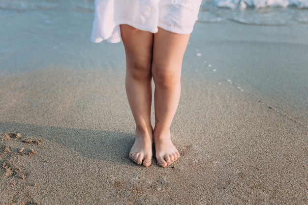 Foto benen van een meisje in een witte jurk op het zandstrand