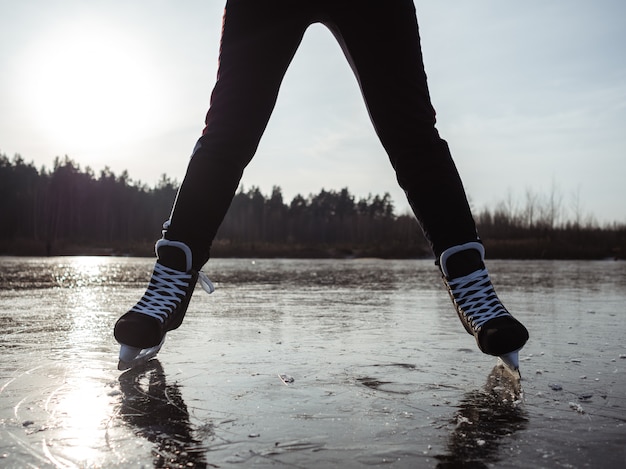 Benen van een meisje op schaatsen spreiden schouderbreedte uit elkaar op het ijs van een meer tegen een bos
