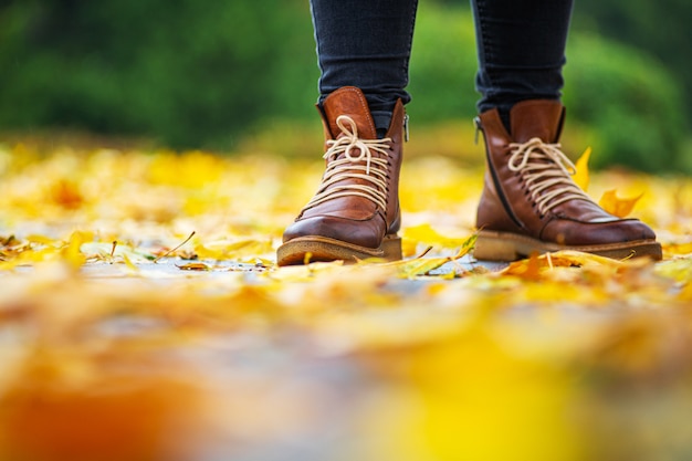 benen van een vrouw in zwarte broek en bruine laarzen in herfst park op stoep bezaaid met gevallen bladeren.