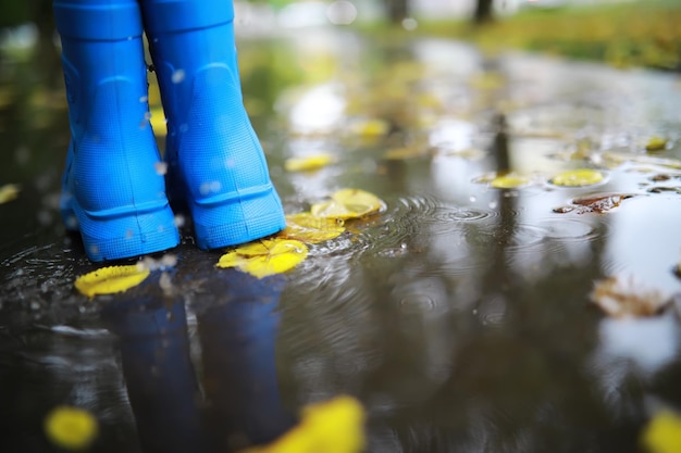 Benen van kind in blauwe rubberen laarzen springen in de herfstplassen