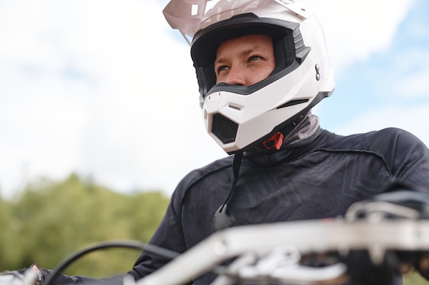 Bepaalde motorrijder in witte helm en jas zittend op de motor en op zoek naar afstand buitenshuis