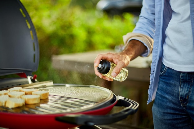 Bereid het ontbijt voor met bruschetta voor het braden van brood en man die olie op de barbecue-gasgrill sproeit