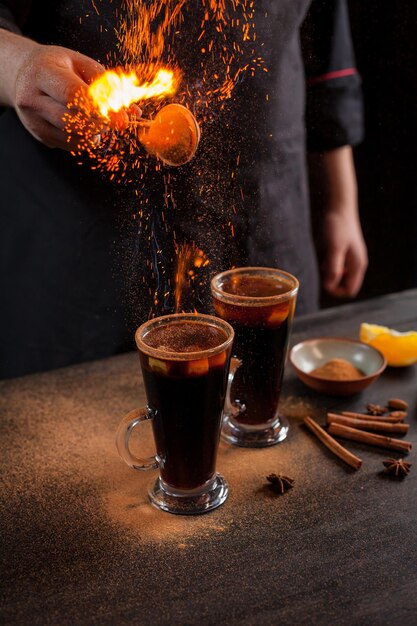 Bereiding van glühwein om te serveren, in een restaurant. Glühwein bij de bereiding van de chef's bar. De handen van de chef-kok op een donkere zwarte achtergrond. Glühwein branden met vonken.