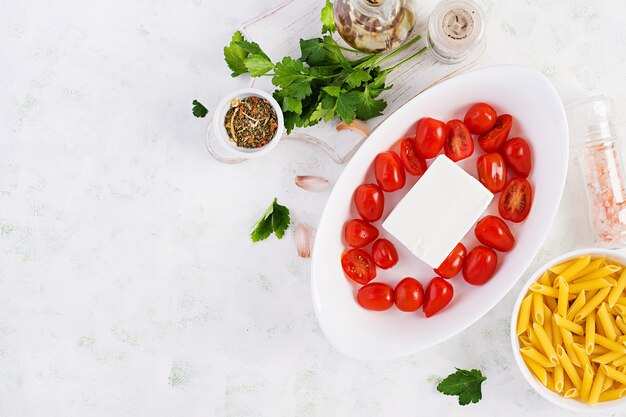 Bereiding van ingrediënten voor fetapasta. Trending Feta bake pasta recept gemaakt van cherrytomaatjes, feta kaas, knoflook en kruiden. Bovenaanzicht, hierboven, kopieer ruimte.