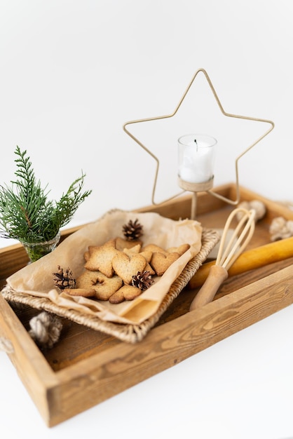 Bereiding van peperkoekkoekjes verschillende peperkoekkoekjes van verschillende vormen liggen op een houten dienblad samen met een sterkaars een garde en een boeket arborvitae Vakantieconcept