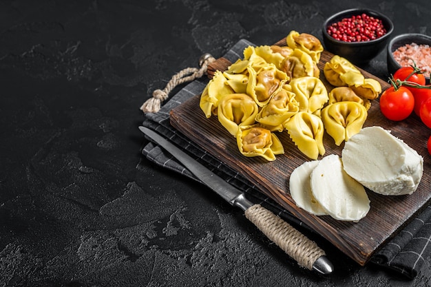 Bereiding van rauwe ravioli met Mozzarella kaas en tomaat. Zwarte achtergrond. Bovenaanzicht. Ruimte kopiëren.