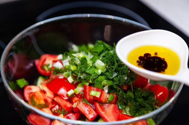 Bereiding van salade van verse groenten, komkommers, tomaten en greens met een witte plastic lepel met een saladedressing gemaakt van olijfolie, balsamicoazijn en sojabonensaus