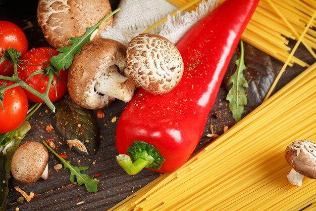 Bereiding van spaghetti pasta met tomaten, knoflook, champignons, peper en olijfolie, op houten tafel