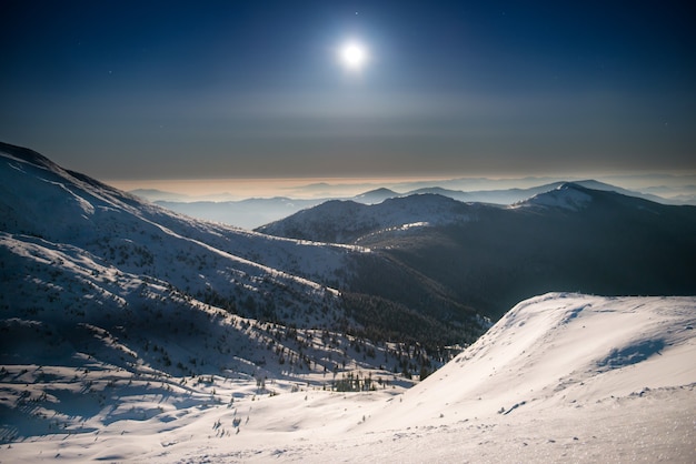 Bereik van winterbergen in witte sneeuw 's nachts onder donkerblauwe lucht met maan en sterren