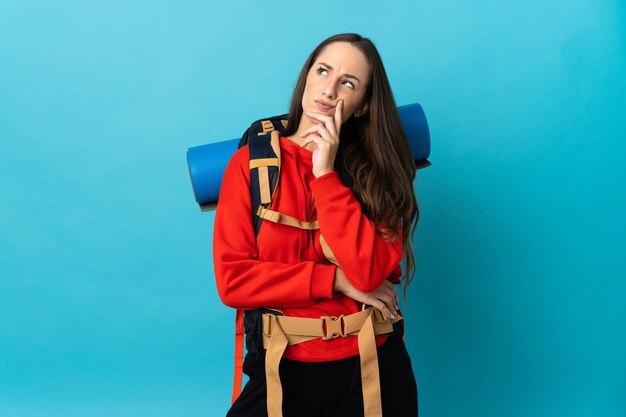 Bergbeklimmer vrouw met een grote rugzak over geïsoleerde achtergrond twijfels tijdens het kijken