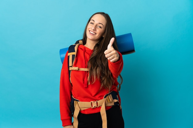 Bergbeklimmer vrouw met een grote rugzak over geïsoleerde muur met duimen omhoog omdat er iets goeds is gebeurd