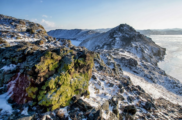 Bergketen met een groene textuur bedekt met sneeuw boven het bevroren meer