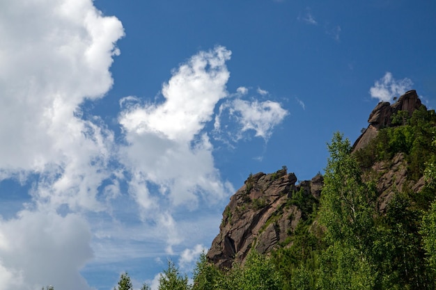 Bergtop met rotsen en bos onder een blauwe lucht met witte wolken