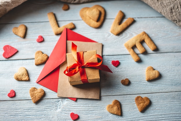 Bericht van een zoet koekje in de vorm van het woord liefde en een geschenk gebonden met een rood lint op een blauwe houten achtergrond