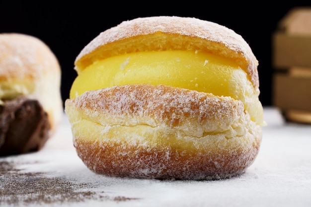 Berlin balls, known as Sonho in Brazil on wooden table with scattered icing sugar. It consists of a fried sweet dough filled with a cream and sugar on top. Selective focus.