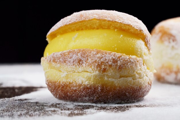 Berlin balls, known as Sonho in Brazil on wooden table with scattered icing sugar. It consists of a fried sweet dough filled with a cream and sugar on top. Selective focus.