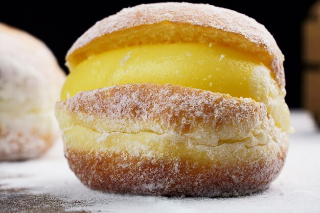 Berlin balls, known as Sonho in Brazil on wooden table with scattered icing sugar. It consists of a fried sweet dough filled with a cream and sugar on top. Selective focus.