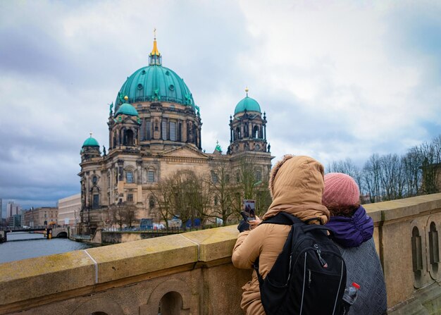 Berlin, Germany - December 8, 2017: Young girls with backpack taking photos on the bridge at Berlin Cathedral near Spree River quay in German City centre in Berlin in Germany in Europe