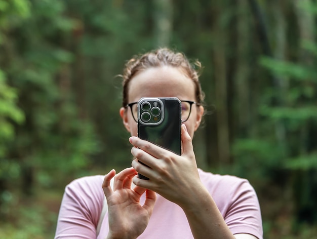 독일 베를린 2023년 7월 15일 휴대폰으로 얼굴을 가리고 자연 속에서 사진을 찍는 여성