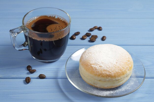 Berliner donut in transparante glasplaat en kopje koffie op blauwe houten tafel close-up