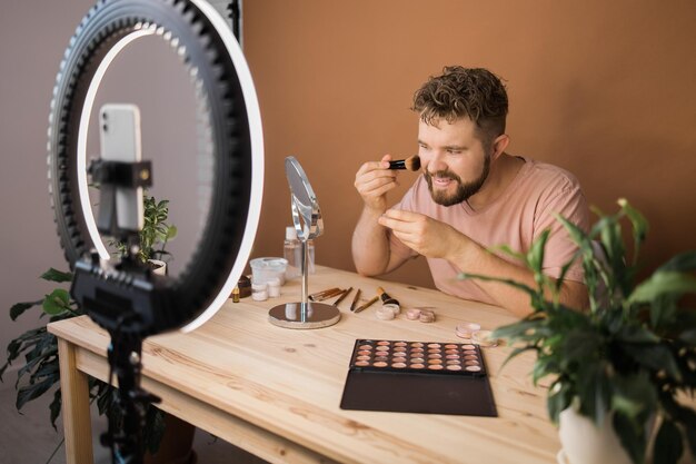 Beroemde blogger Vrolijke mannelijke vlogger die cosmeticaproducten laat zien terwijl hij video opneemt en advies geeft voor zijn beautyblog Visagist en beautyvlog-concept opneemt