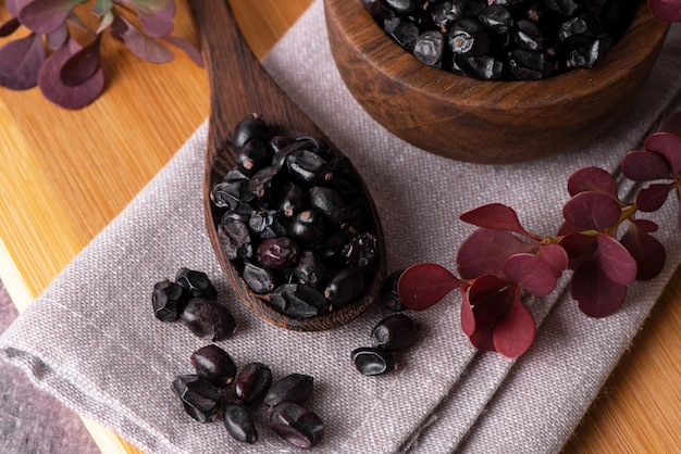 Berries of black barberry in wooden bowl and spoon Spice barberry blue Dry berries of barberries