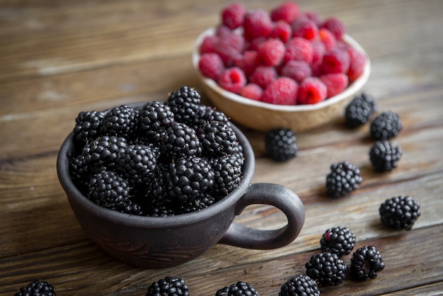 Berries blackberries and raspberries with ceramic dishes stand on the table.